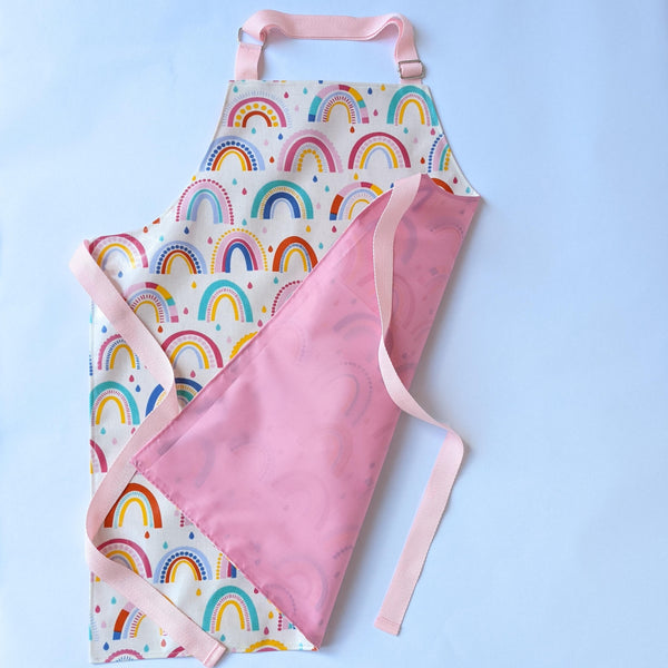 Medium, Lined, Wipeable, Kids Rainbow Oilcloth Apron with front pocket and baby pink adjustable neck band and waist ties and trim.