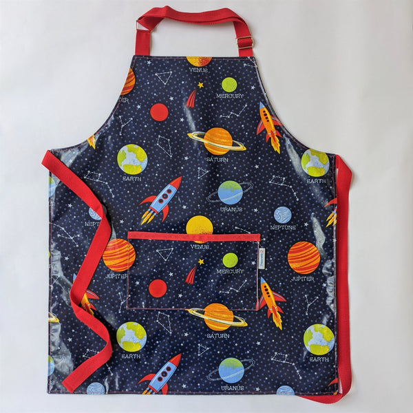 Large, lined, wipeable, kids Space Oilcloth Apron with front pocket,  Red Adjustable neck band and red ties and trim.