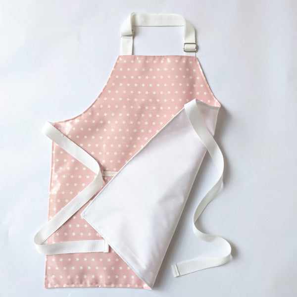 Small, lined, wipeable, kids Twinkle Pink Oilcloth Apron with front pocket and white adjustable neck band and waist ties.