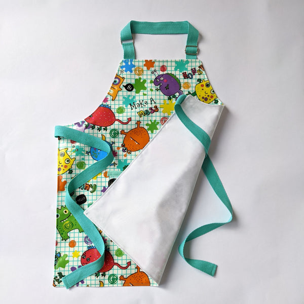 Small, lined, wipeable, kids Monster oilcloth apron with front pocket and adjustable neck band and aqua waist ties.